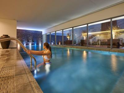 Woman entering a modern, illuminated indoor pool with large glass windows.