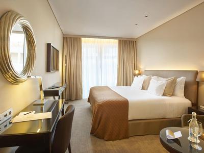 Bright hotel room with double bed, desk, chair, and large window with curtains.