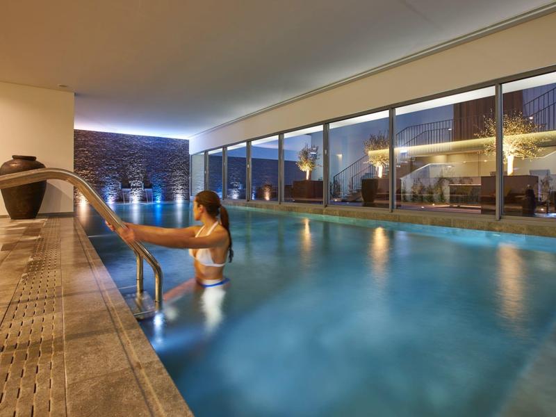 Woman entering a modern, illuminated indoor pool with large glass windows.