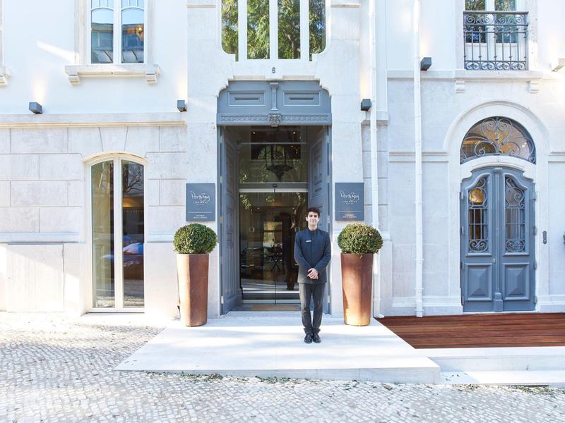 Person walking out of an elegant hotel with white facade and blue doors.