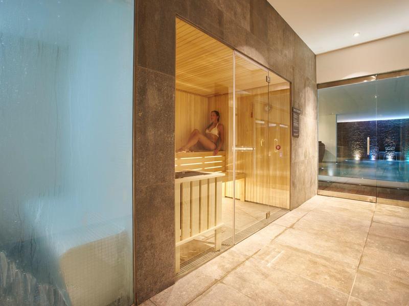 Modern wellness area with sauna and view of a pool area at night.