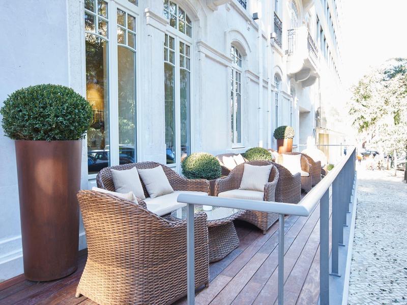 Cozy terrace with wicker chairs and small tables in front of a hotel building.