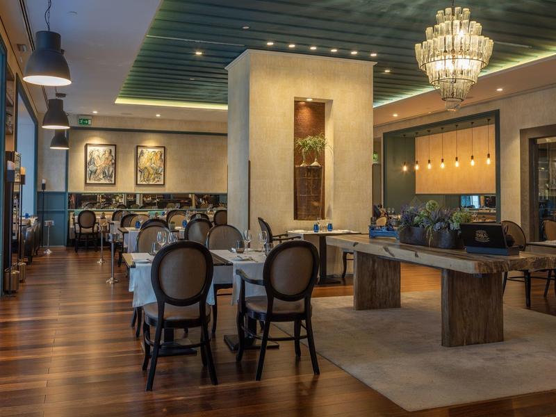 Elegant restaurant with wooden floor, black chairs, and chandeliers.