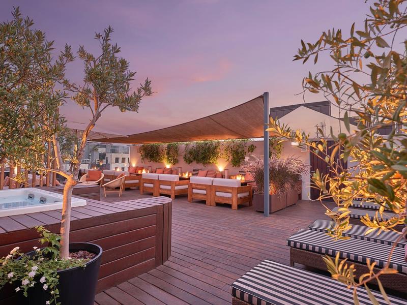 Cozy rooftop terrace with seating, plants, and illuminated hot tub at dusk