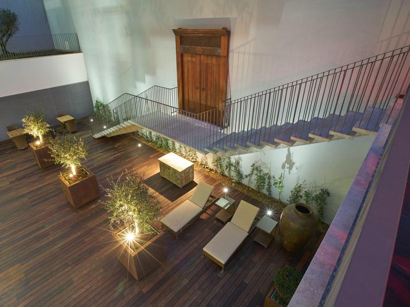Modern hotel terrace outdoor area with wooden deck, sun loungers, and plants at dusk.