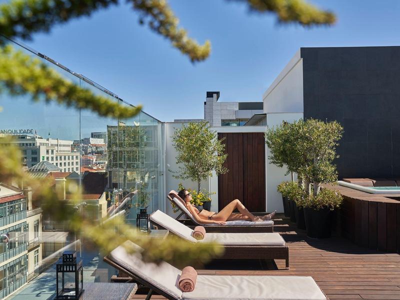 Rooftop terrace with lounge chairs, plants, and city views under clear sky