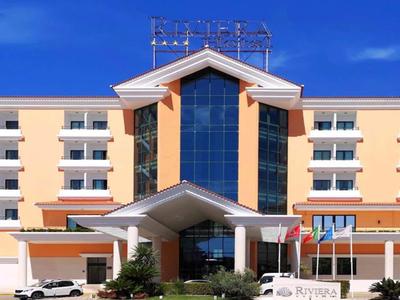 Edificio moderno de hotel con fachada naranja y blanca y gran ventana de vidrio central bajo cielo azul.
