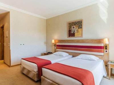 Habitación de hotel con dos camas individuales, cubrecamas rojos, paredes claras y suelo de madera.