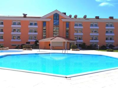 Großes Hotelgebäude mit oranger Fassade und klarem blauen Pool im Vordergrund bei sonnigem Himmel.