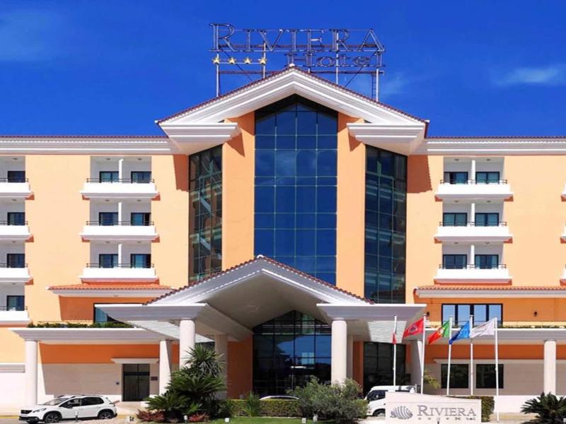 Edificio moderno de hotel con fachada naranja y blanca y gran ventana de vidrio central bajo cielo azul.