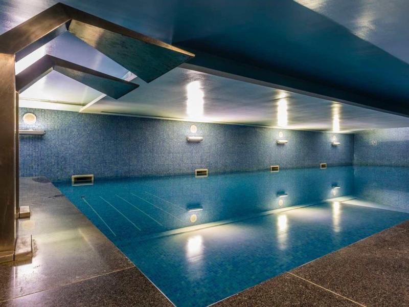 Piscina interior moderna con paredes azules y ducha de acero inoxidable en el área de bienestar de un hotel.