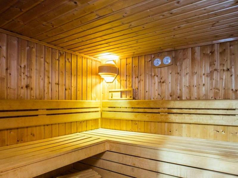 Sauna de madera clara con bancos curvos y luz cálida montada en la pared.
