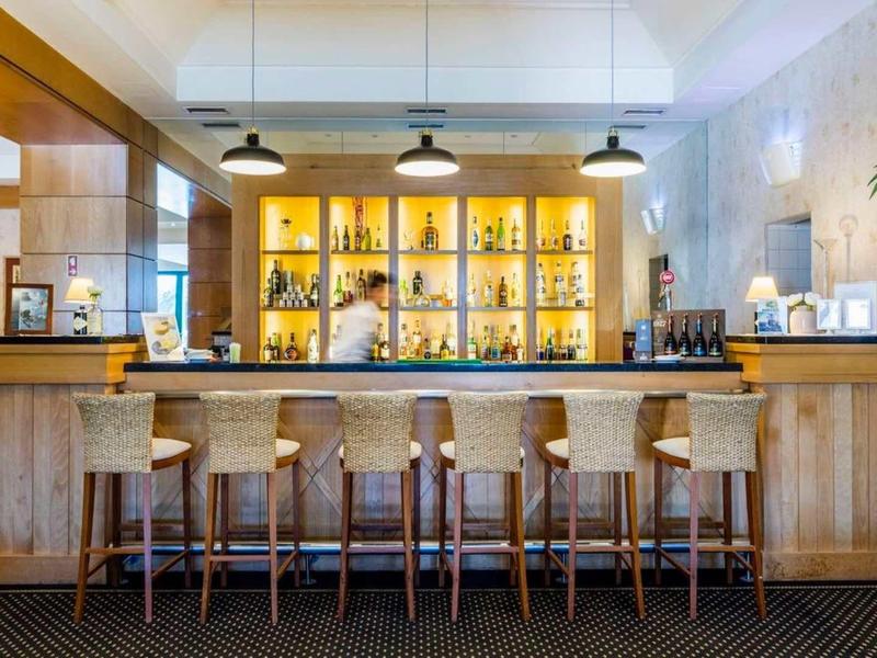 Área de bar luminosa en hotel con cinco taburetes de madera frente a barra antigua y estanterías iluminadas.