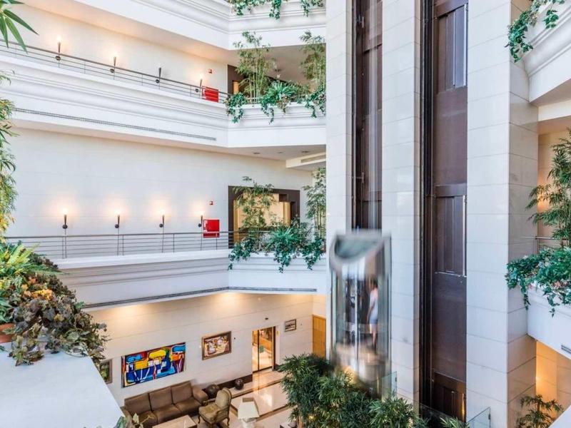 Espacioso interior de hotel iluminado con balcones de varios pisos y muchas plantas.