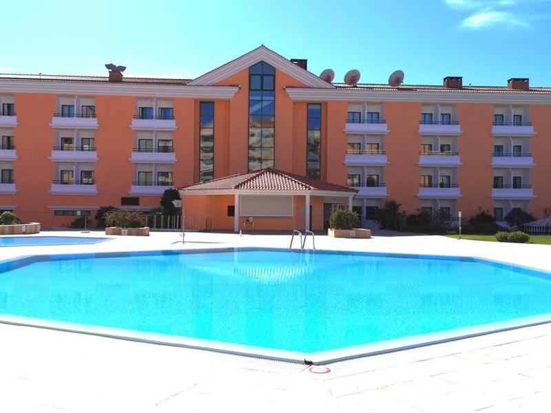 Hotel con edificio naranja y piscina exterior azul clara bajo cielo soleado.