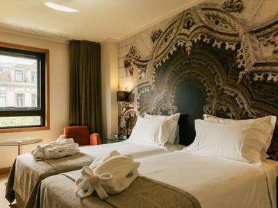 Elegant hotel room with two single beds, decorative wall design, and natural daylight.