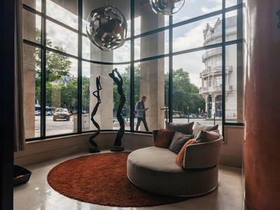 Modern hotel lobby seating area with panoramic windows, sculptures, and round chairs.