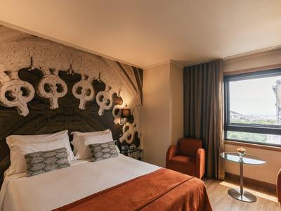 Modern hotel room with double bed, decorative headboard, and view through the window.