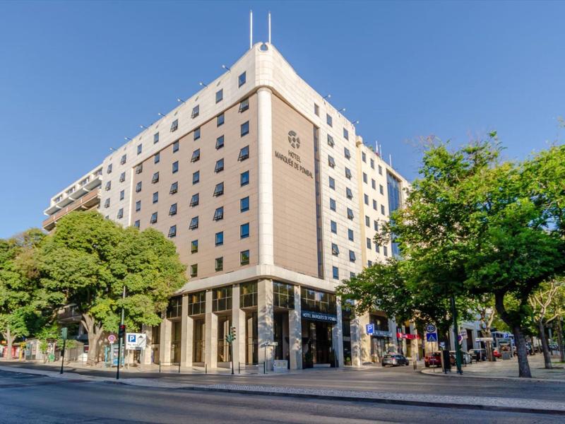 Modern hotel building on a street corner with trees and clear sky.
