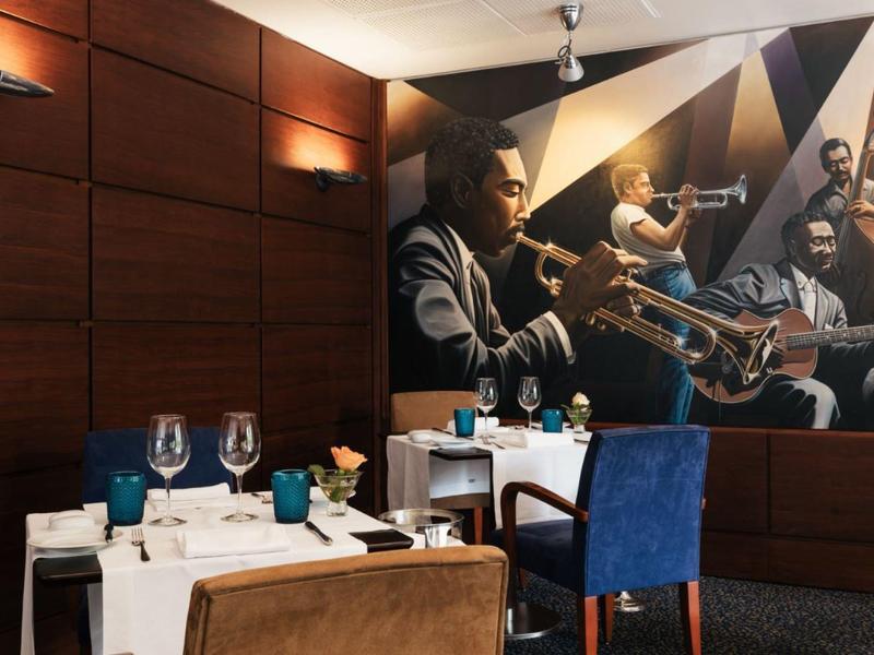 Modern dining area with blue and brown chairs and wall art featuring jazz musicians.