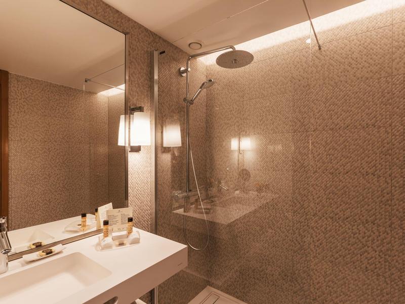 Modern bathroom with large shower, white sink, and soft lighting.