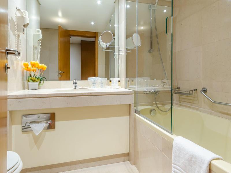 Modern hotel bathroom with sink, shower, and bathtub in cream-colored design.