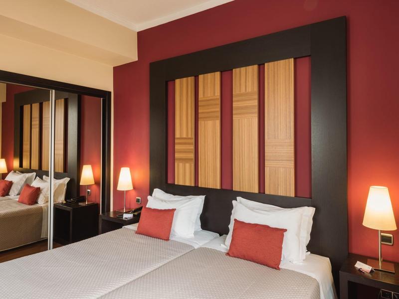 Camera d'albergo moderna con due letti, accenti rossi e un grande specchio.