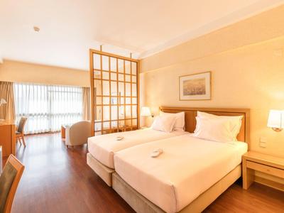 Camera d'hotel luminosa con due letti singoli, pavimento in legno e divisorio davanti alla finestra.