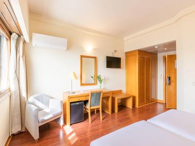 Camera d'hotel luminosa con letto matrimoniale, scrivania, sedia e finestra con tende.