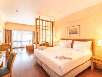 Camera d'hotel luminosa con letto matrimoniale, pavimento in legno e grande finestra con tende.