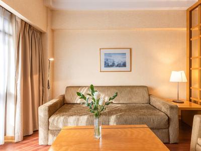 Soggiorno luminoso con divano, vaso di vetro su tavolo in legno e grande finestra con tende.