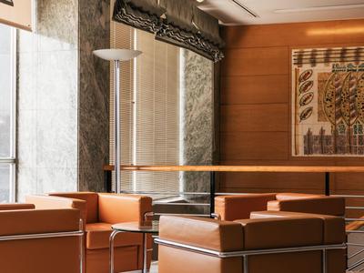 Lounge d'hotel moderna con poltrone in pelle marrone, rivestimenti in legno e grande opera d'arte al muro.