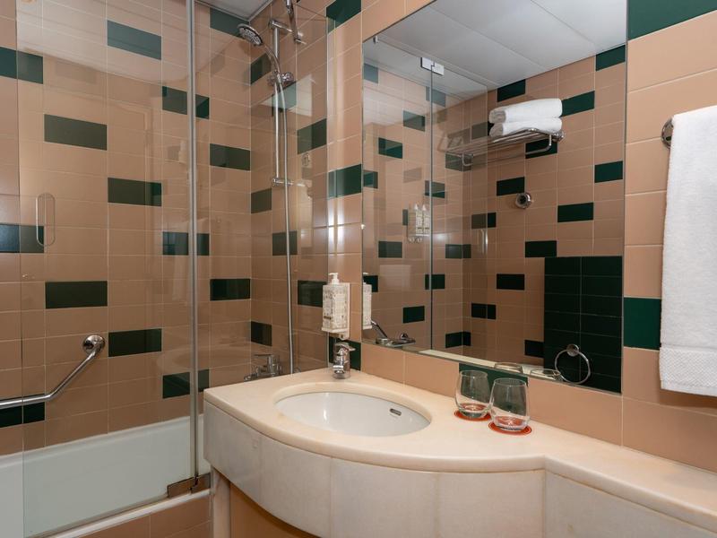 Bagno moderno con doccia, lavabo e asciugamano in tonalità beige e verde.