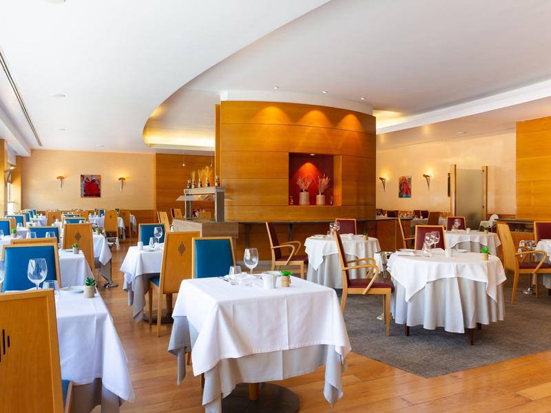 Ristorante d'hotel elegante con tavoli apparecchiati di bianco e interni caldi in legno.
