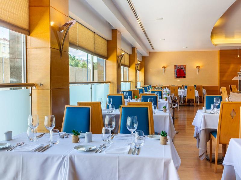 Ristorante elegante con tovaglie bianche e sedie blu, ambiente luminoso e soleggiato.
