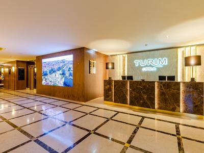 Area reception moderna dell'hotel con banco illuminato e grande schermo.