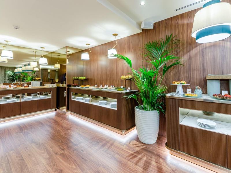 Buffet in hotel con pannelli in legno e piante in vasi bianchi.