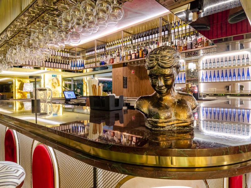 Bar elegante dell'hotel con busto dorato e banco stiloso con scaffalature in vetro.