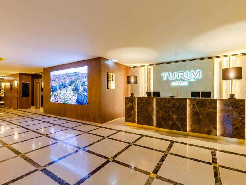 Area reception moderna dell'hotel con banco illuminato e grande schermo.