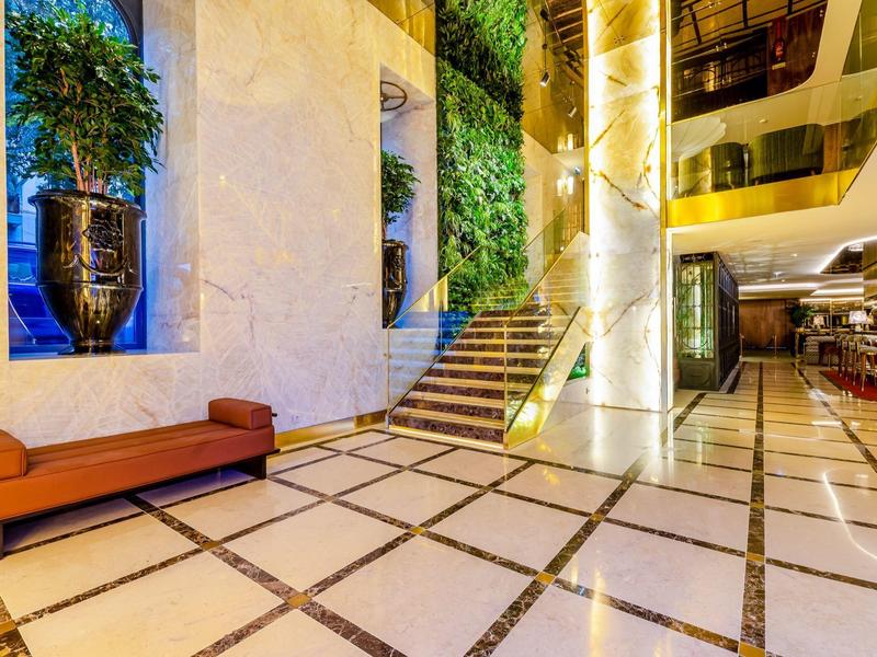Atrio di hotel luminoso con pavimento in marmo, scale e arredi moderni.