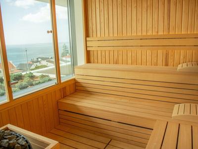 Sauna z drewnianą ścianą i stopniowymi ławkami z widokiem na morze przez duże okno.