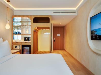 Nowoczesny pokój hotelowy z łóżkiem podwójnym, telewizorem i minimalistycznym drewnianym wystrojem.