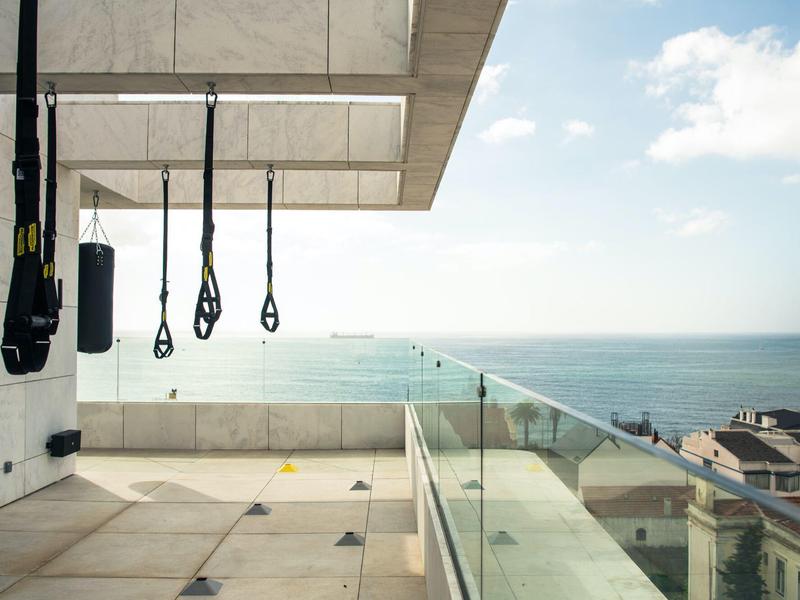 Nowoczesna siłownia na balkonie z widokiem na morze i pasami treningowymi.