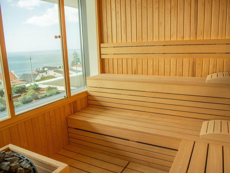 Sauna z drewnianą ścianą i stopniowymi ławkami z widokiem na morze przez duże okno.