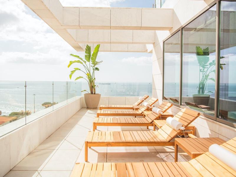 Nowoczesny taras z drewnianymi leżakami i widokiem na morze w słoneczny dzień.