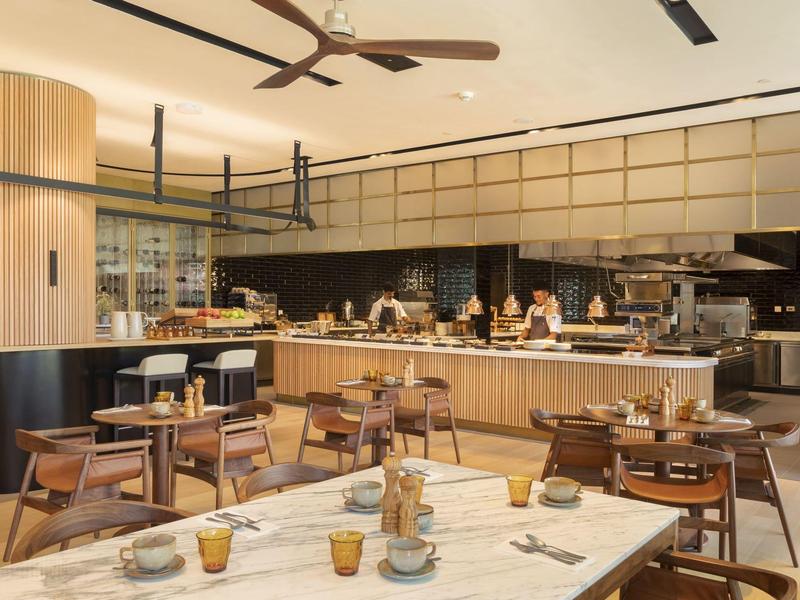 Nowoczesna restauracja hotelowa z drewnianymi i marmurowymi akcentami, stołami i otwartą kuchnią.