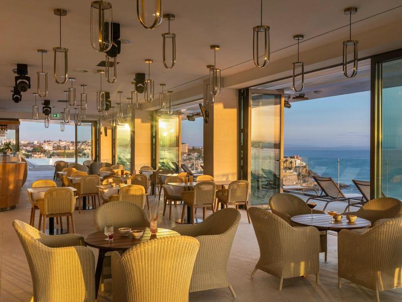 Elegancka restauracja hotelowa z panoramicznym widokiem na morze o zachodzie słońca.