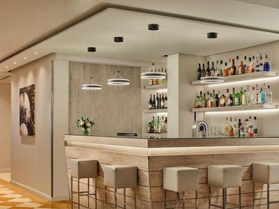 Moderner Hotelbarbereich mit bequemen Hockern, beleuchteten Regalen und zeitgenössischer Dekoration.