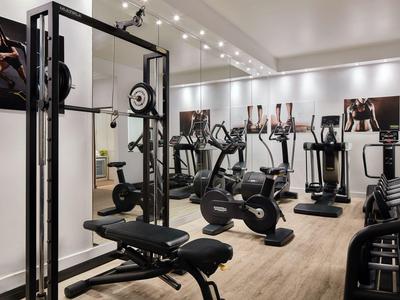 Moderner Fitnessraum mit verschiedenen Trainingsgeräten und Spiegelwand in hellem Ambiente.