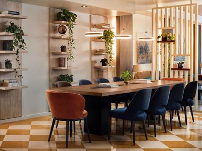 Modern eingerichteter Essbereich mit langem Holztisch, verschiedenfarbigen Stühlen und Pflanzen.